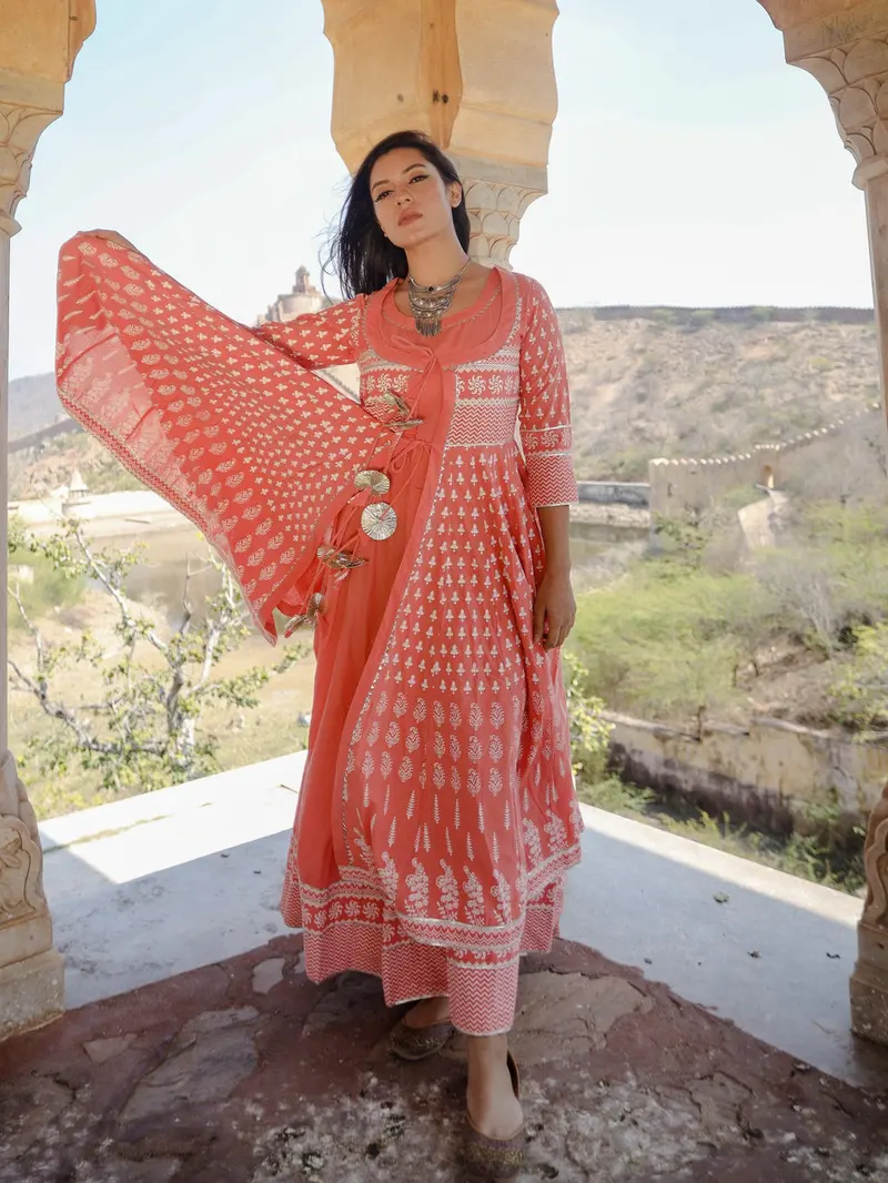 Woman in an orange block-print cotton Anarkali dress and dupatta, standing on a stone terrace